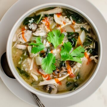 A white bowl filled with miso chicken and rice soup that is garnished with sriracha sauce and a cilantro sprig.