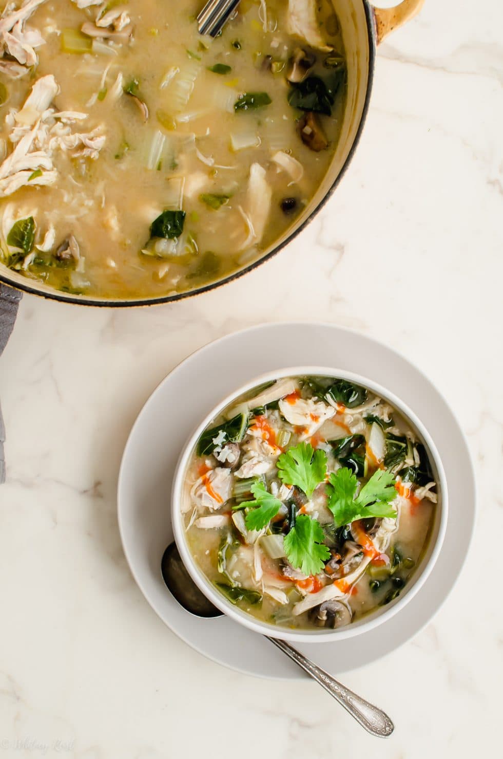 A white bowl filled with miso chicken and rice soup that is garnished with sriracha sauce and a cilantro sprig.