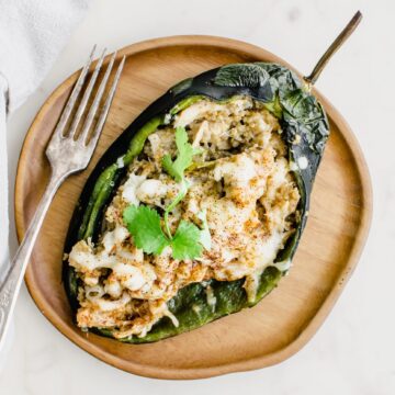 An overhead shot of a wooden plate with a stuffed poblano peppers and fork on the side.