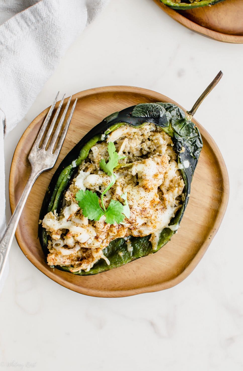 An overhead shot of a wooden plate with a stuffed poblano peppers and fork on the side. 