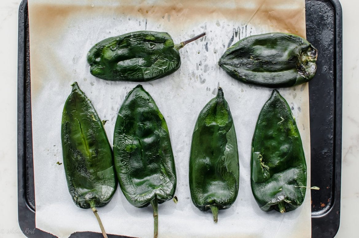 A baking sheet lined with parchment paper with roasted poblano peppers on top.