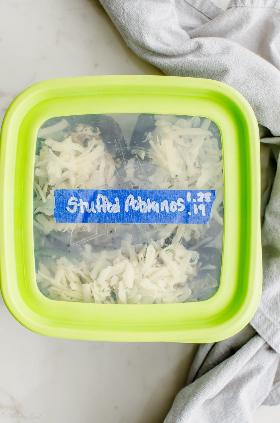 A freezer container filled with stuffed poblano peppers with a date and name label.