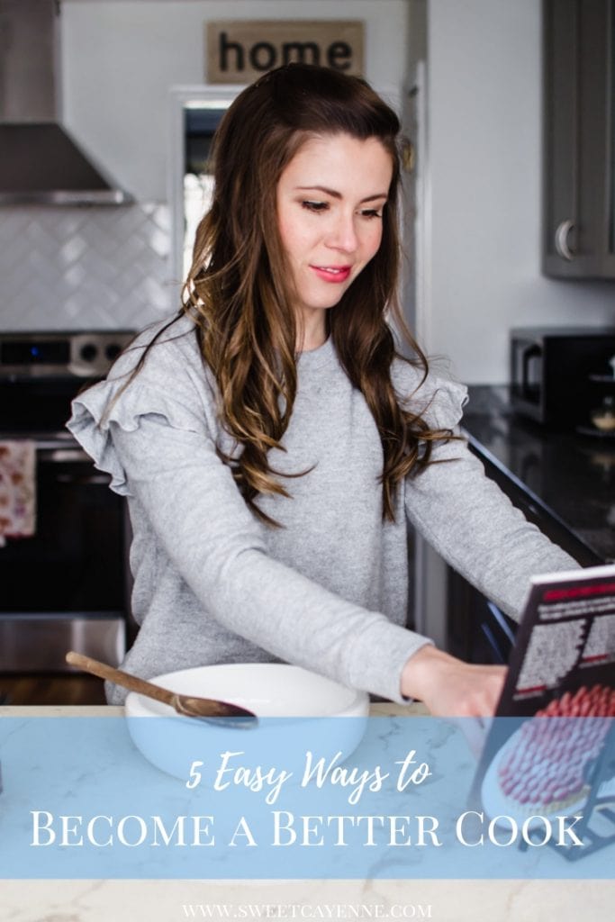 A brunette woman reading a cookbook at a white marble counter with a mixing bowl on top.