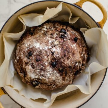 A yellow Dutch oven with a chocolate rye boule inside.