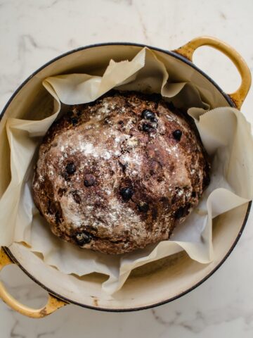 A yellow Dutch oven with a chocolate rye boule inside.