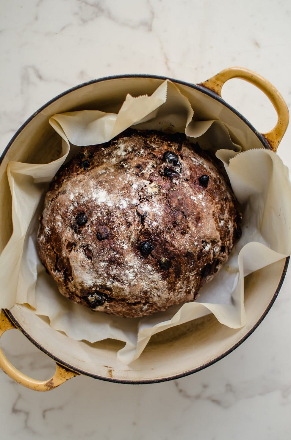 A yellow Dutch oven with a chocolate rye boule inside. 