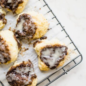 A wire rack with a sheet of parchment paper on top and cinnamon biscuits.