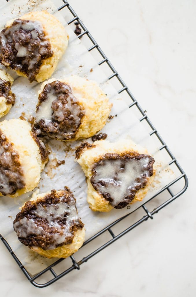 A wire rack with a sheet of parchment paper on top and cinnamon biscuits. 