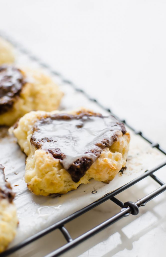 A wire rack with a sheet of parchment paper on top and cinnamon biscuits.