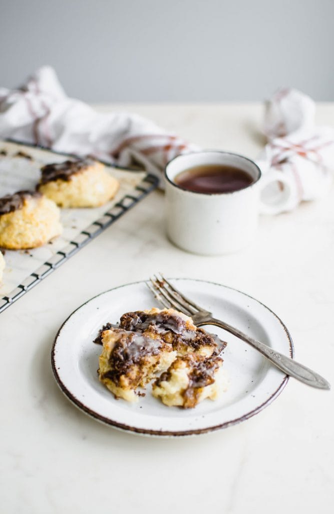 A white plate with a cinnamon drop biscuit and a cup of tea on the side. 