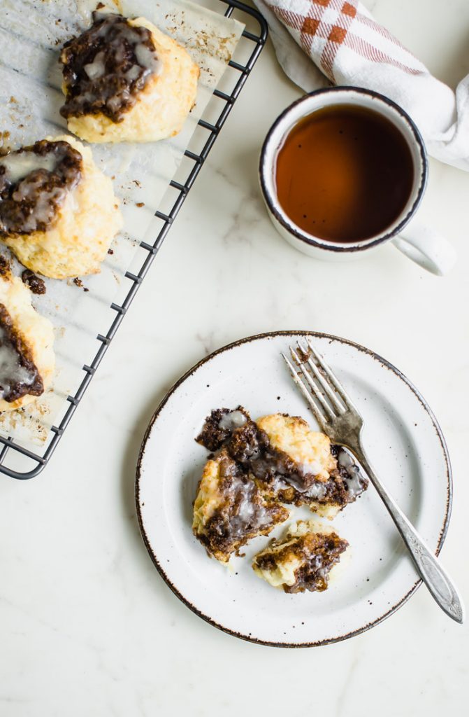 A white plate with a cinnamon drop biscuit and a cup of tea on the side. 