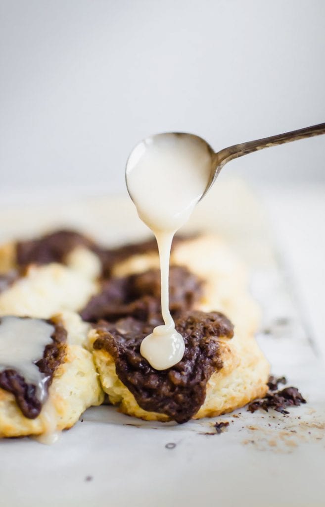 A spoon drizzling vanilla glaze over a cinnamon drop biscuit.