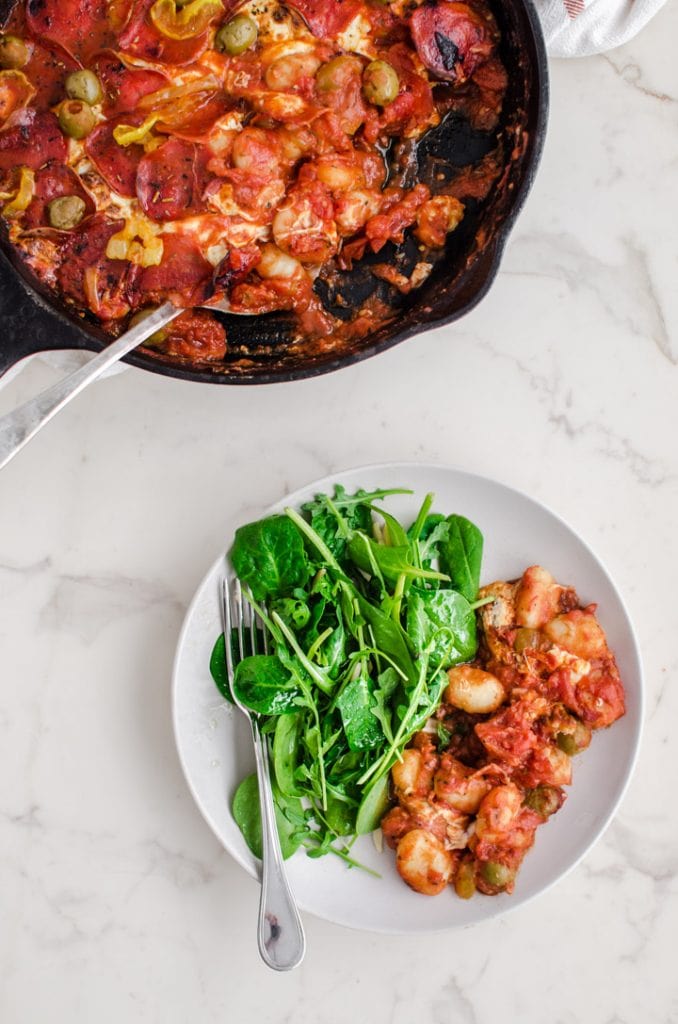 A white plate with a serving of pizza baked gnocchi and a side salad.