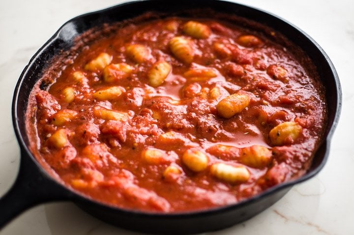 A cast iron skillet with tomato sauce and gnocchi.