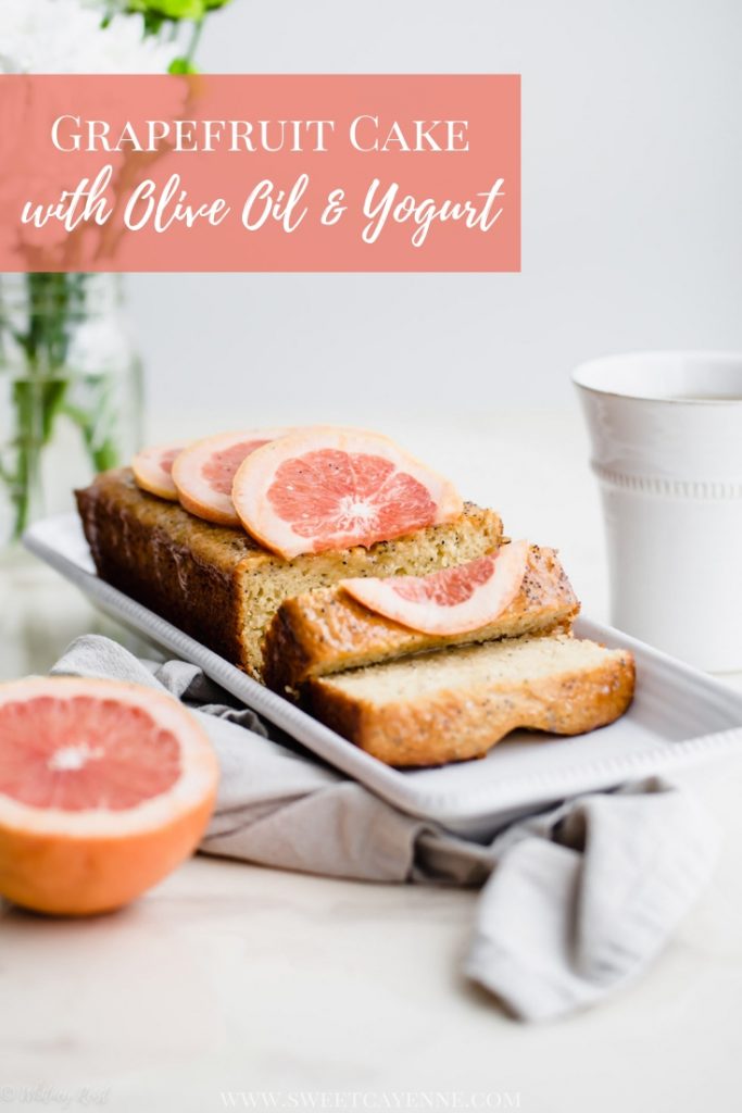 A loaf of sliced grapefruit cake on a white platter with flowers and a cup of tea on the side.