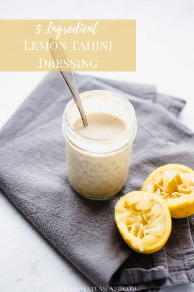 A jar of lemon tahini sauce on a gray towel with juiced lemons on the side.