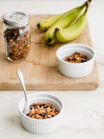 A cutting board with granola, a glass of milk, and bananas.