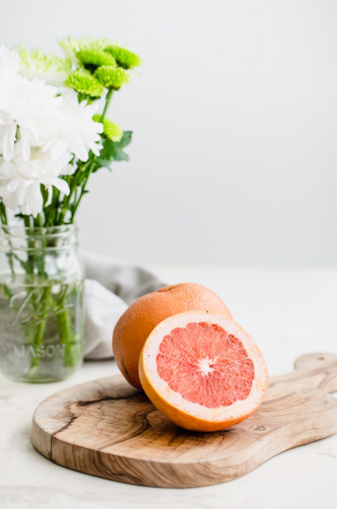 A sliced grapefruit on a cutting board with flowers on the side. 