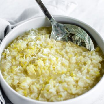 A side shot of a bowl of lemon risotto with a spoon on the side.