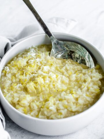 A side shot of a bowl of lemon risotto with a spoon on the side.