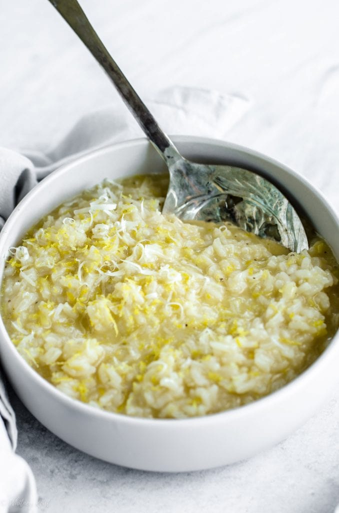 A side shot of a bowl of lemon risotto with a spoon on the side. 