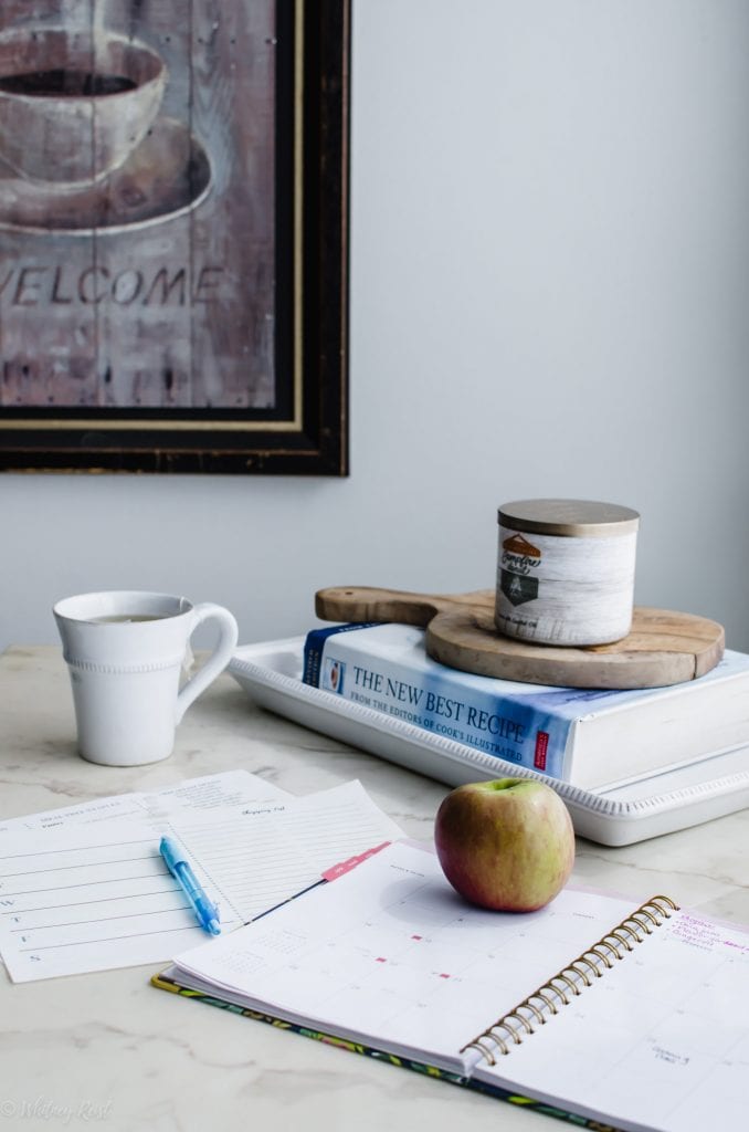 Menu planning sheets with a planner and apple on a white marble counter.