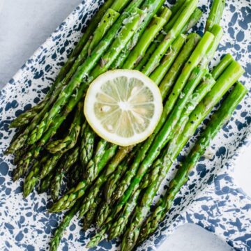 A blue and white tray with roasted asparagus and a lemon slice on top.