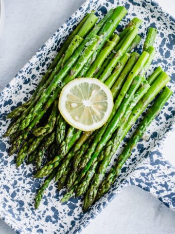 A blue and white tray with roasted asparagus and a lemon slice on top.
