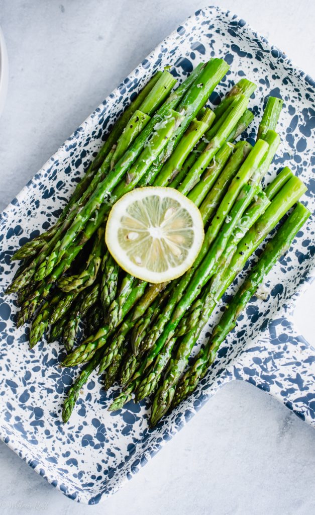 A blue and white tray with roasted asparagus and a lemon slice on top.