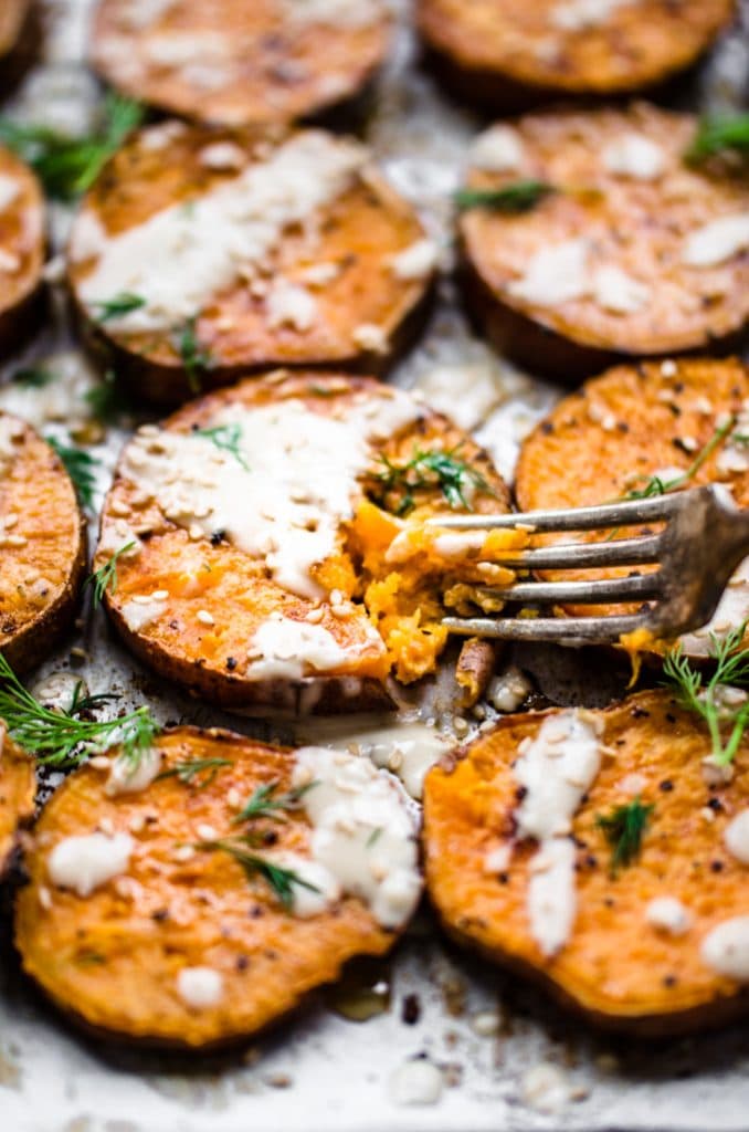 A fork slicing into a round of roasted sesame sweet potatoes on a baking sheet.