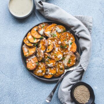 A grey plate with roasted sesame sweet potatoes on a blue concrete backdrop.