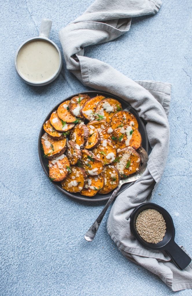 A grey plate with roasted sesame sweet potatoes on a blue concrete backdrop.