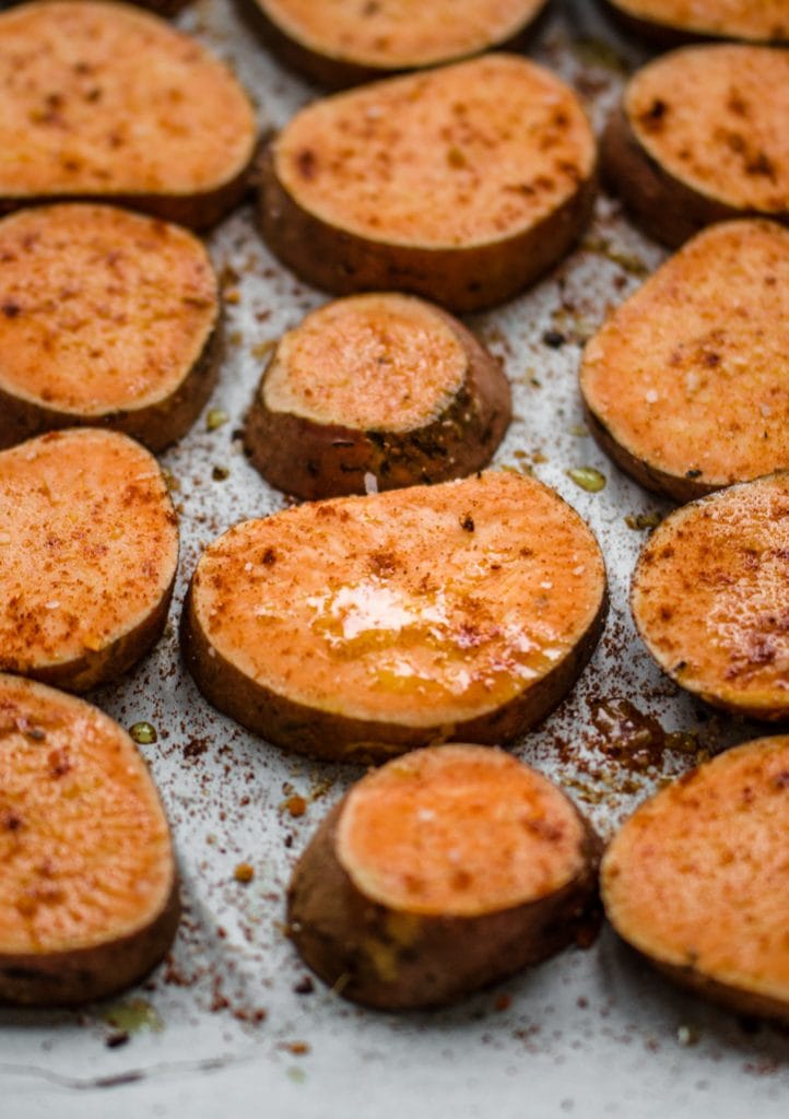 Round pieces of sweet potato on a baking sheet sprinkled with spices and olive oil.