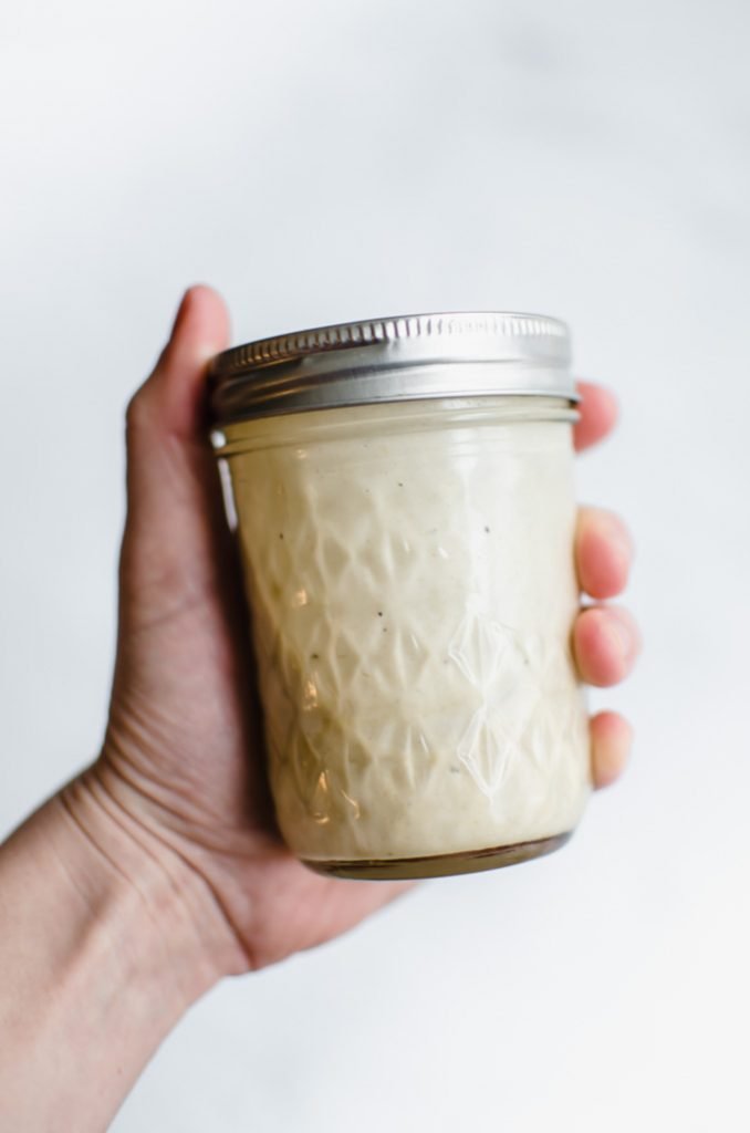 A hand holding a jar of lemon tahini dressing. 