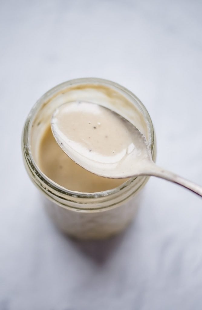 A spoon over a jar with lemon tahini dressing. 