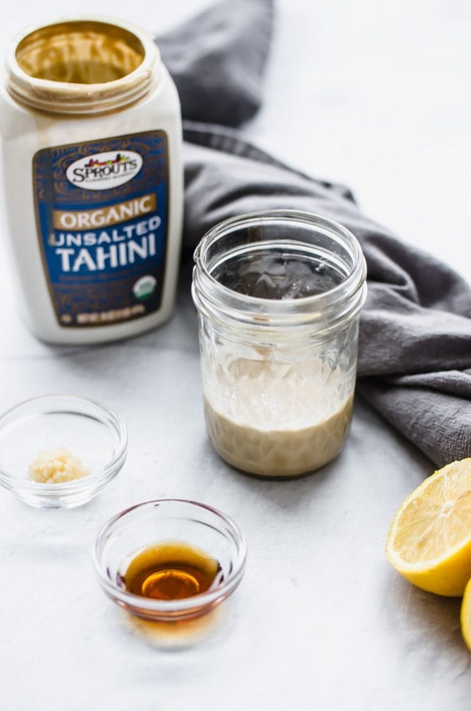 A jar of lemon tahini sauce on a gray towel with juiced lemons on the side. 