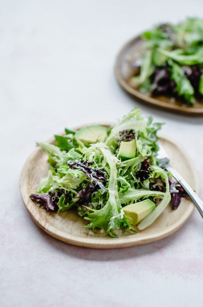 A wooden plate with everyday springtime salad on top with a fork on the side.