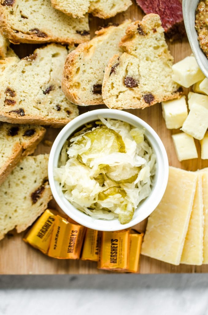 A close up of a white dish of sauerkraut on a charcuterie board.