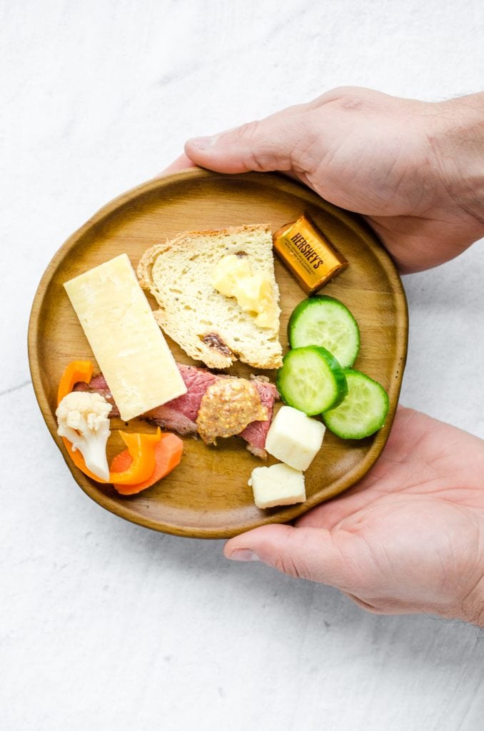 Two hands holding a wooden plate with appetizers on it. 