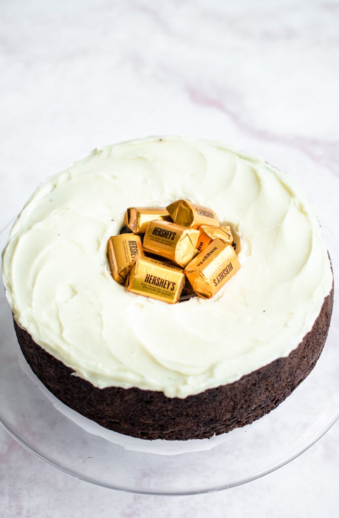 A chocolate cake with cream cheese frosting and a Hershey's gold nuggets in the center.