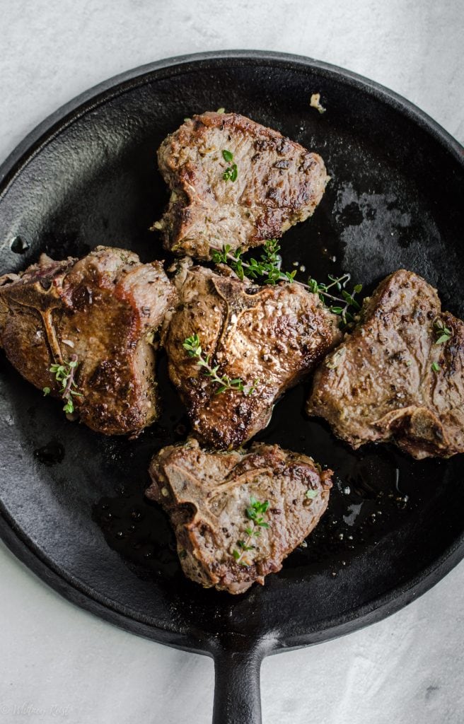 A cast iron griddle with lamb chops and fresh thyme.