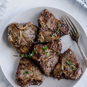 A white plate with pan seared lamb chops and a fork.