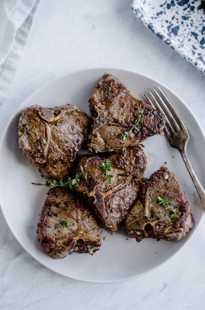 A white plate with pan seared lamb chops and a fork. 