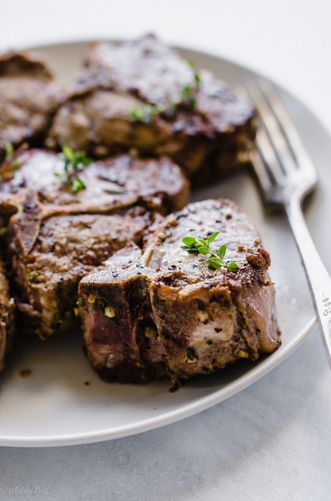 A side shot of Tuscan grilled lamb chops on a white plate with a fork on the side. 