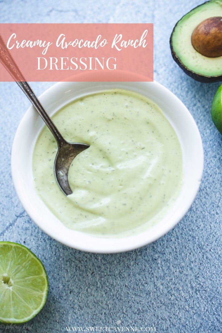 A white bowl filled with creamy avocado ranch dressing on a blue stone counter with limes on the side.