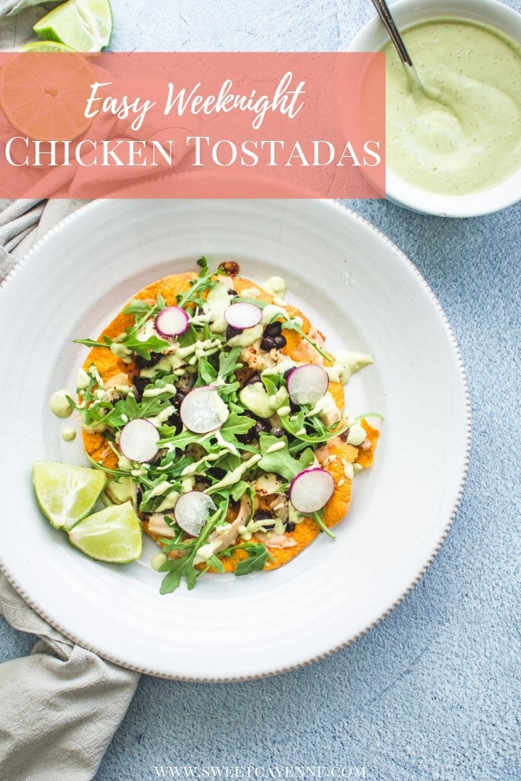 An overhead shot of a chicken tostada on white plate with lime wedges and a bowl of avocado ranch on the side. 