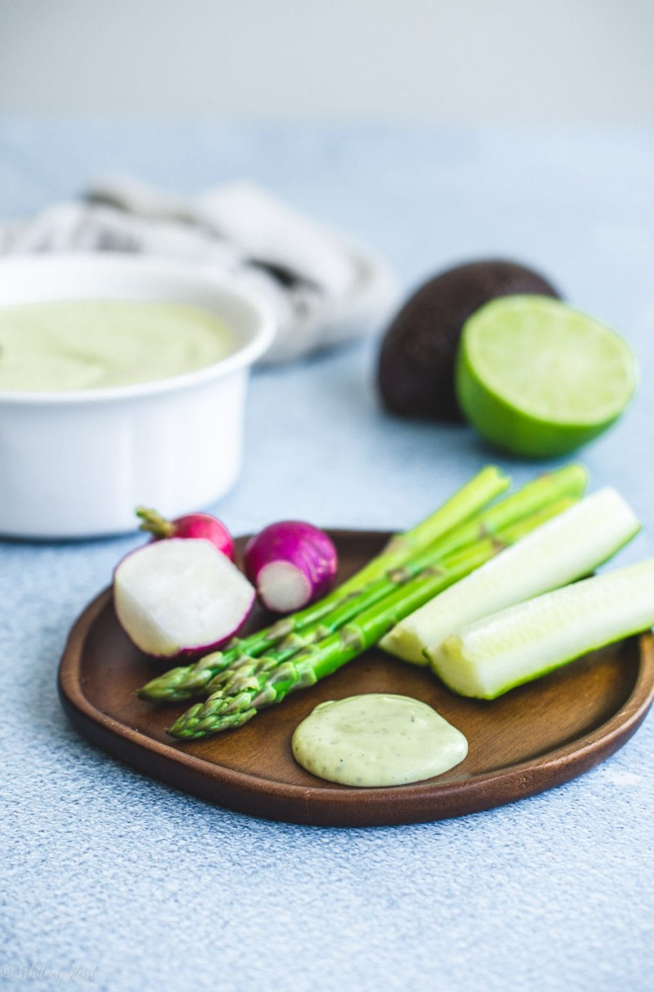 A wooden plate with veggie sticks and creamy avocado ranch dressing.