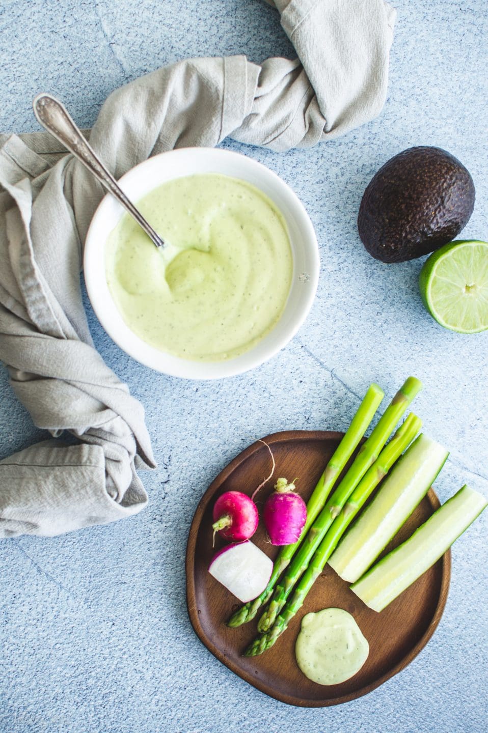 A wooden plate with veggie sticks and creamy avocado ranch dressing.