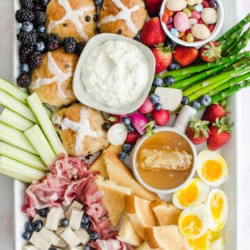 A white rectangle platter filled with items for an Easter brunch grazing board against a pink marble background.