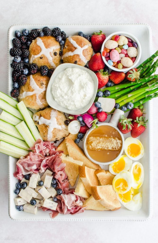 A white rectangle platter filled with items for an Easter brunch grazing board against a pink marble background.